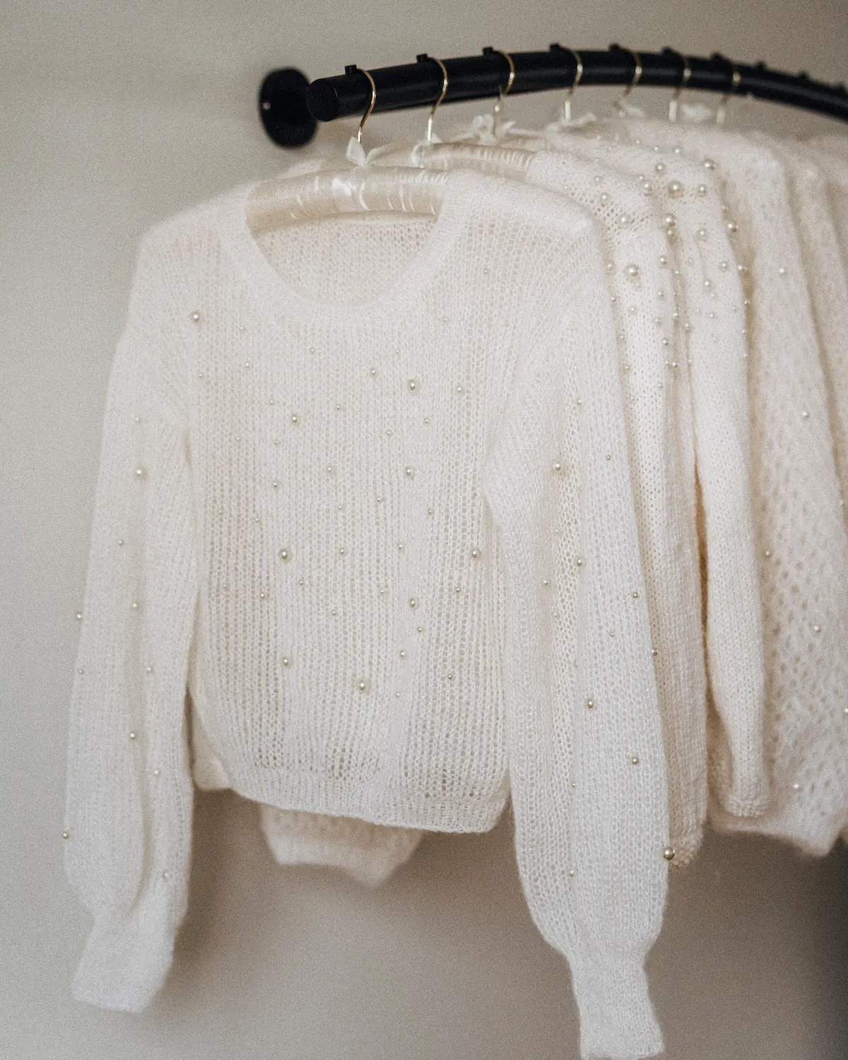 Weiße Strickpullover mit Perlenbesatz hängen ordentlich auf Kleiderbügeln.